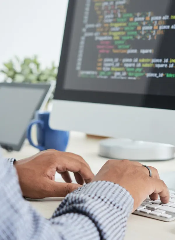 Close-up of a computer screen displaying code, with a staff member at work, typing on the keyboard.